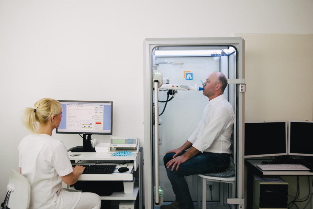 Lungenfunktionsprüfung mit Patient in der Messkabine der Praxis Dr. Maschek.